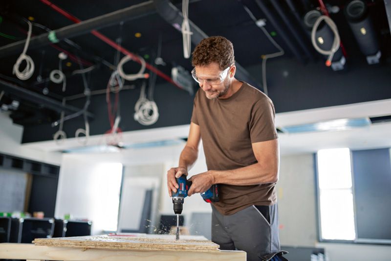 En person iført sikkerhedsudstyr borer i et panel på en byggeplads.